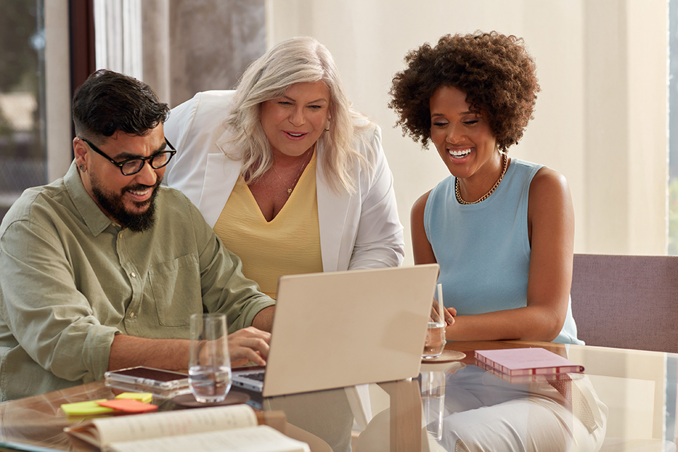 Três Consultores de Beleza Natura e Avon, um homem, e duas mulheres, em reunião, sorrindo e olhando para tela de um notebook.