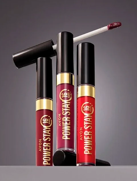 Três batons líquidos Power Stay da Avon, em tons diferentes, com aplicadores e a assinatura Avon.