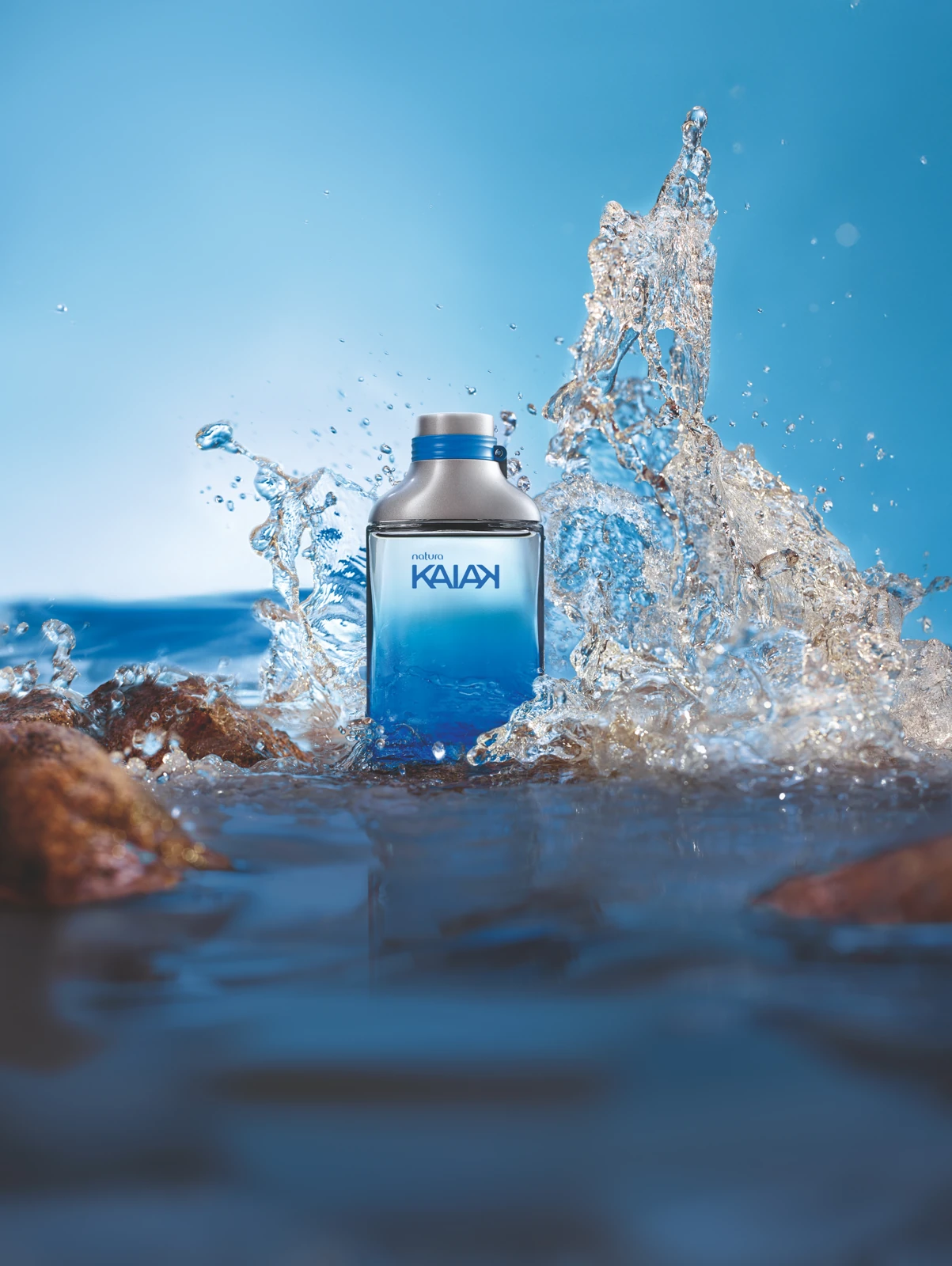Frasco azul do desodorante colônia Kaiak da Natura cercado por água, com a assinatura Natura.
